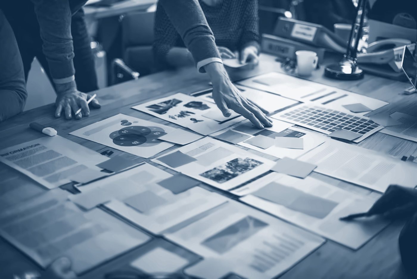 Hands arranging plans, charts and notes across a table